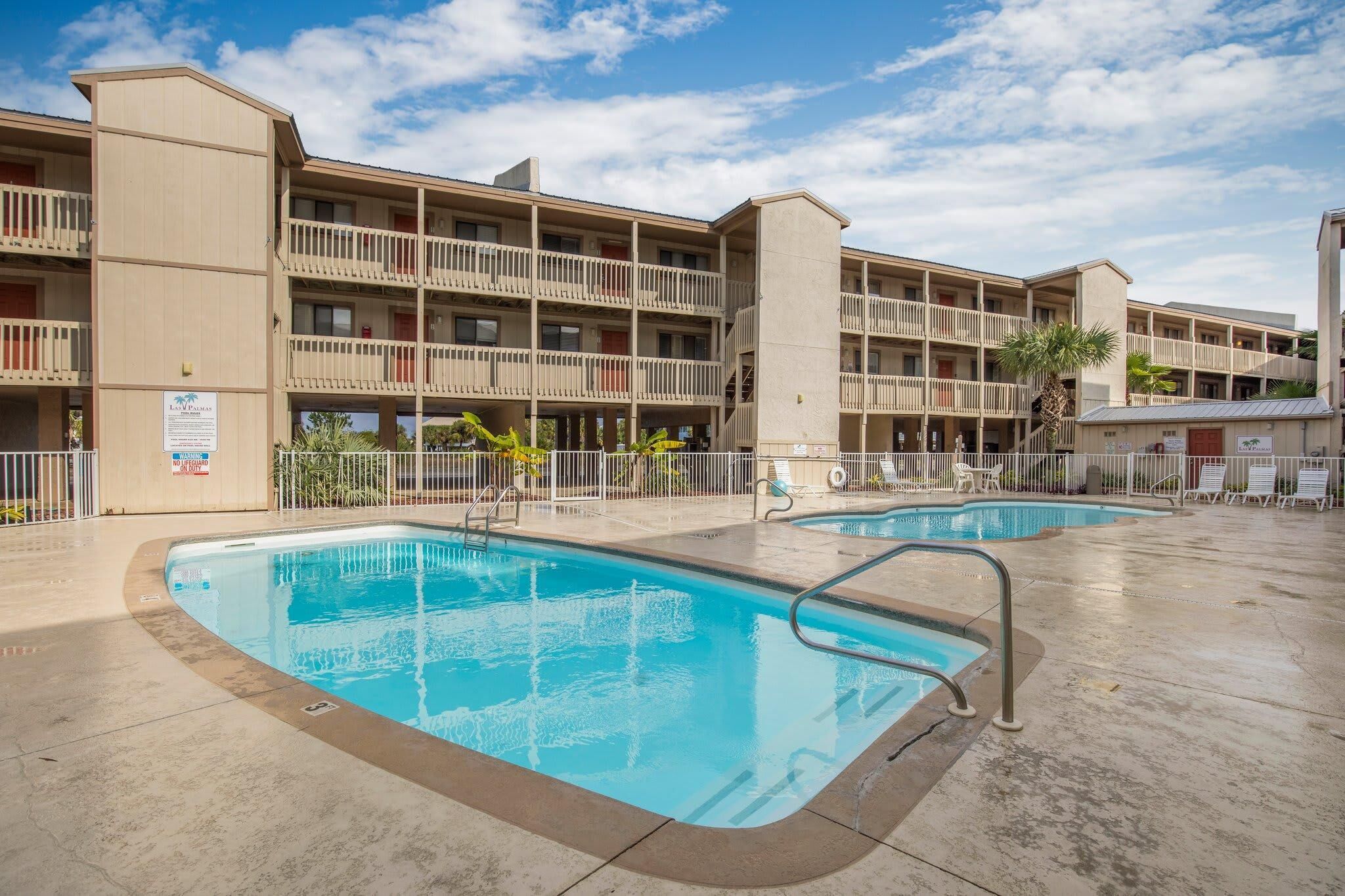 A hotel with a pool area, multiple balconies, and a clear sky.