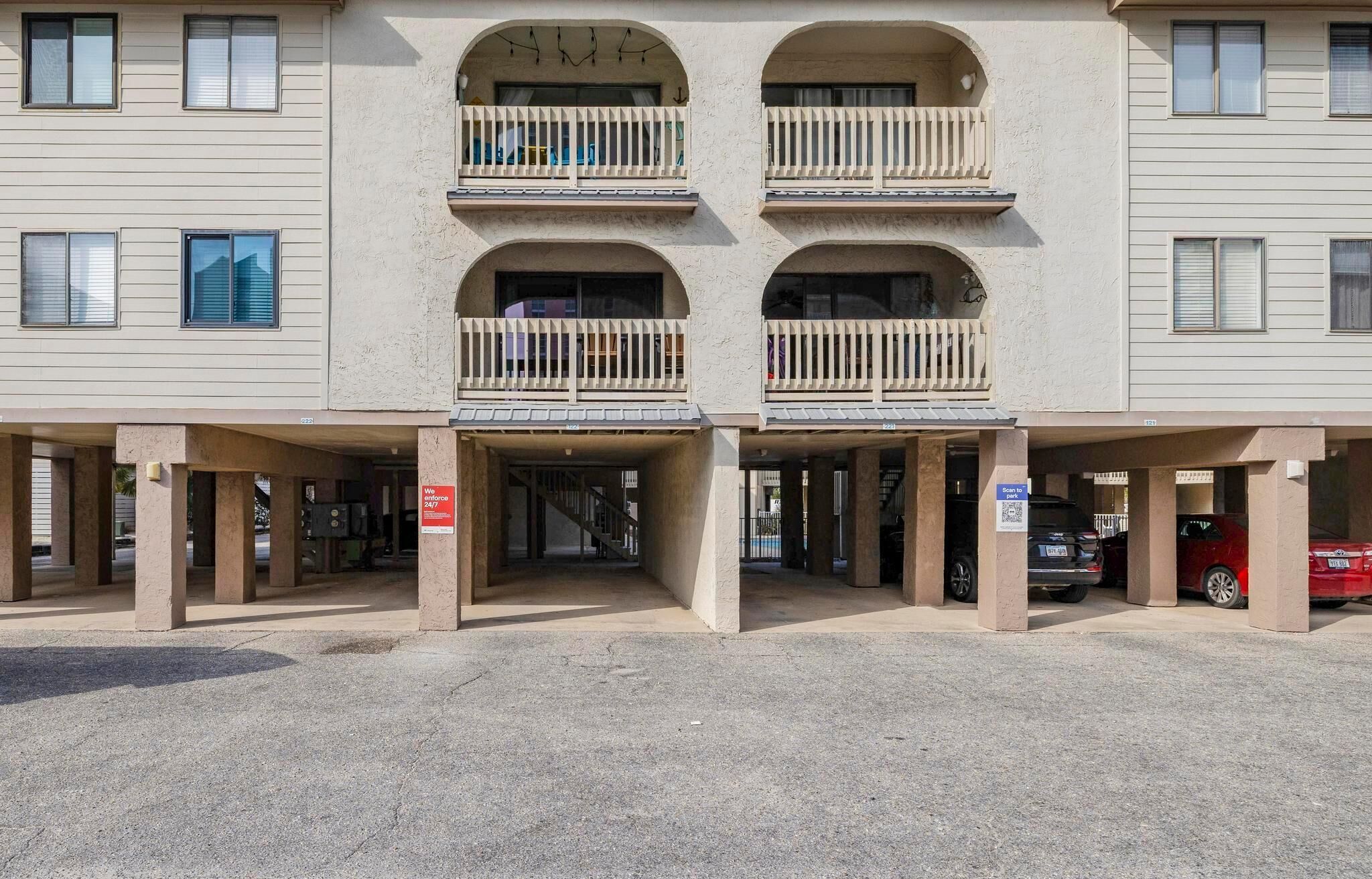 A multi-story building with a central entrance, balconies, and a parking area.