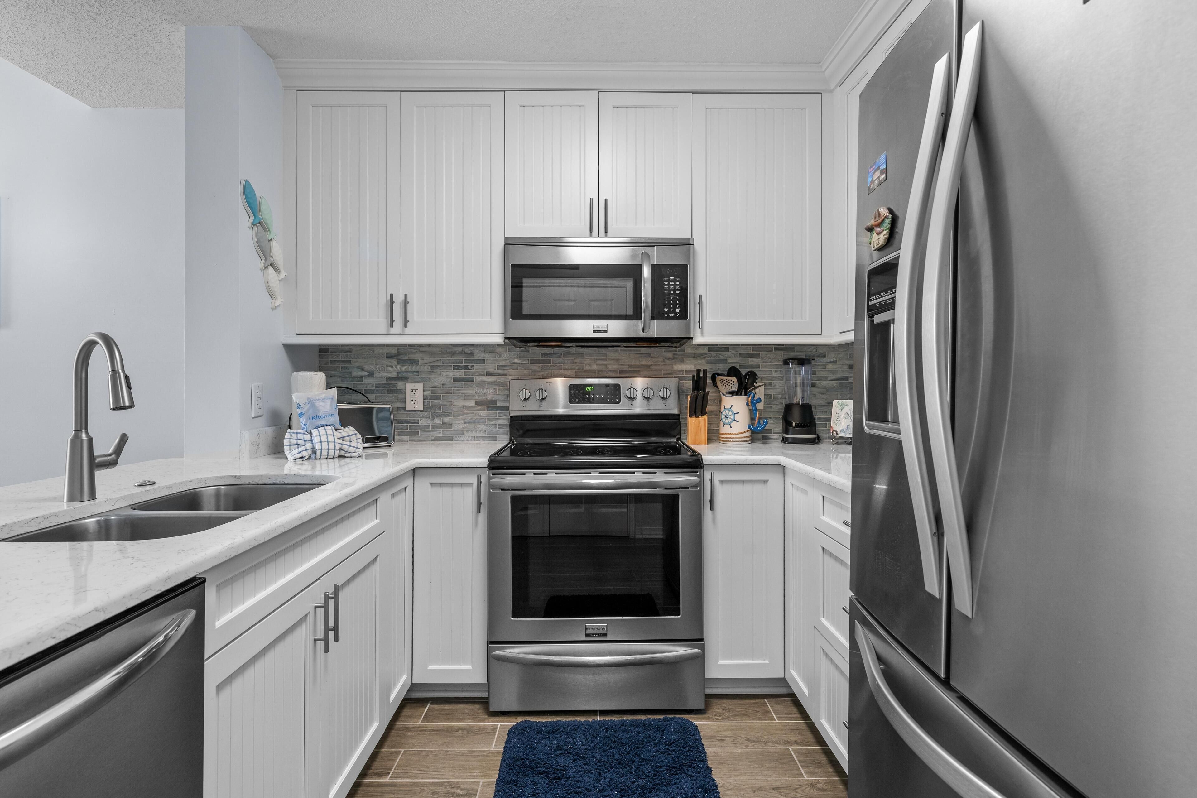 A modern kitchen with white cabinets, stainless steel appliances, a double sink, and a blue rug.