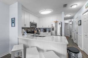 Una cocina moderna con armarios blancos, electrodomésticos de acero inoxidable y una isla central con taburetes de bar.