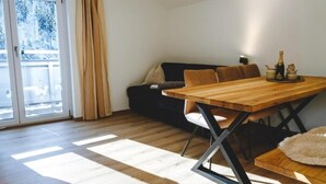 Ruokailutila, jossa on puinen pöytä ja tuolit, sohva sekä näkymä lasiovesta.