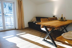 A dining area with a wooden table and chairs, a sofa, and a view through a glass door. - Alpen Haus Maria/Chalet (Viehhofen)