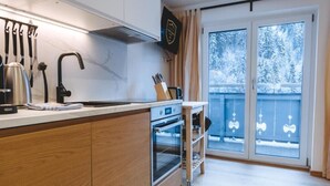 Moderni keittiö, jossa on puiset kaapit, ruostumattomasta teräksestä valmistetut kodinkoneet ja näkymä lumiselle parvekkeelle.