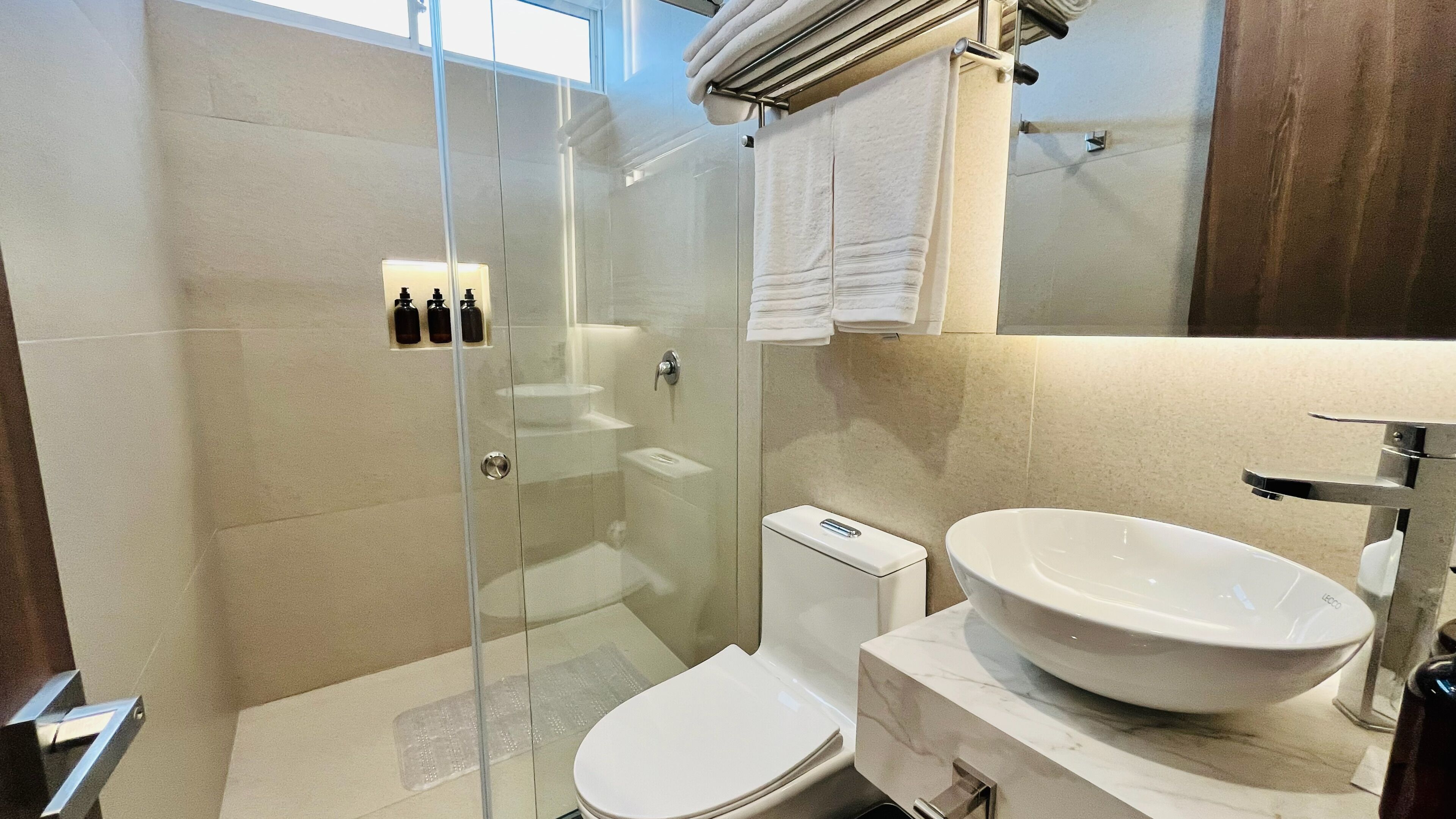 A modern bathroom with a glass shower enclosure, a white toilet, and a large sink with a mirror above it.