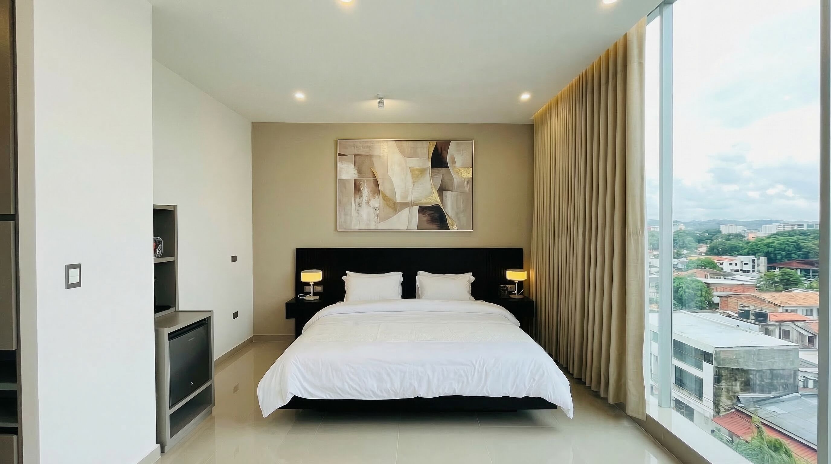 Una habitación de hotel moderna con una cama grande, un cuadro en la pared y vistas a la ciudad.