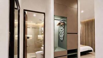 Una habitación de hotel moderna con vestidor, cama y baño visible a través de una puerta abierta.