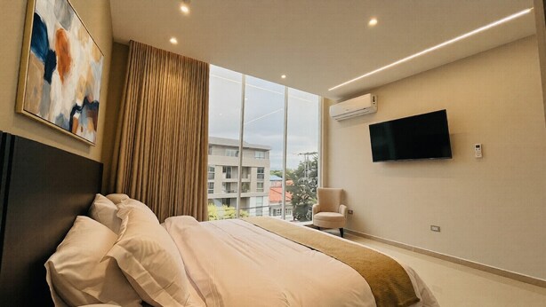 A modern hotel room with a large bed, a flat-screen TV, an air conditioning unit, and a view of the outside. - Hotel Murahno (San Jose de Cucuta)