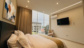 A modern hotel room with a large bed, a flat-screen TV, an air conditioning unit, and a view of the outside. - Hotel Murahno (San Jose de Cucuta)