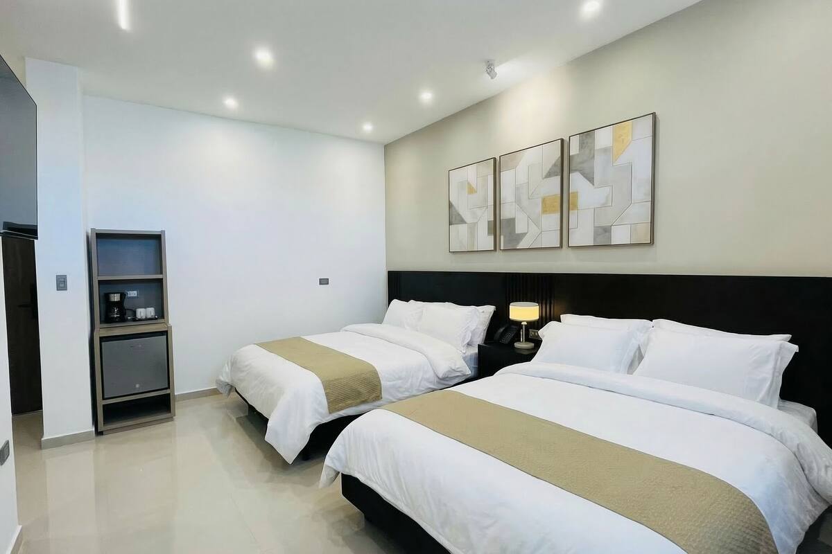A hotel room with two beds, a minibar, a flat-screen TV, and abstract wall art.