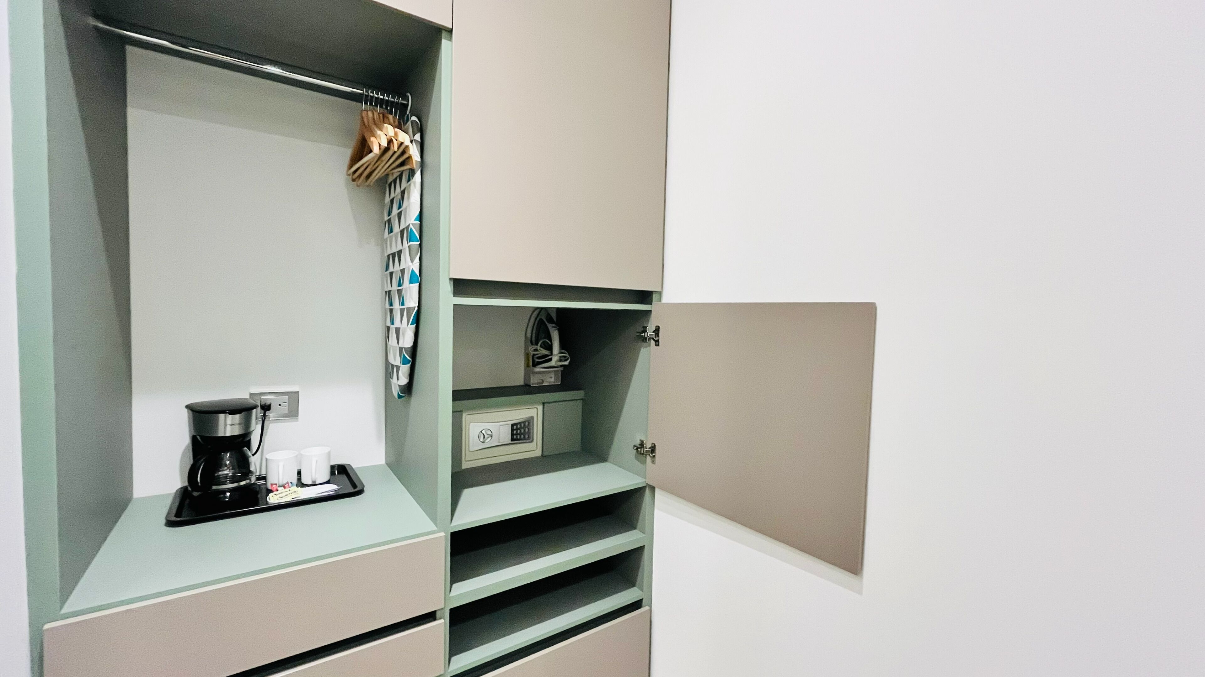 Una kitchenette con cafetera, dos tazas, un tendedero con utensilios y un mueble pequeño con cerradura.