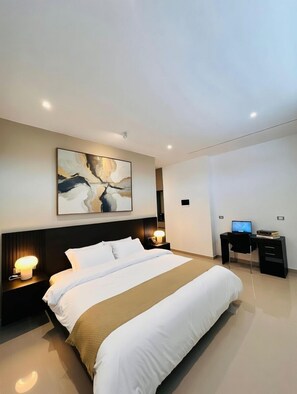 Una habitación de hotel moderna con una cama grande, un escritorio con ordenador y un cuadro abstracto colgado en la pared.