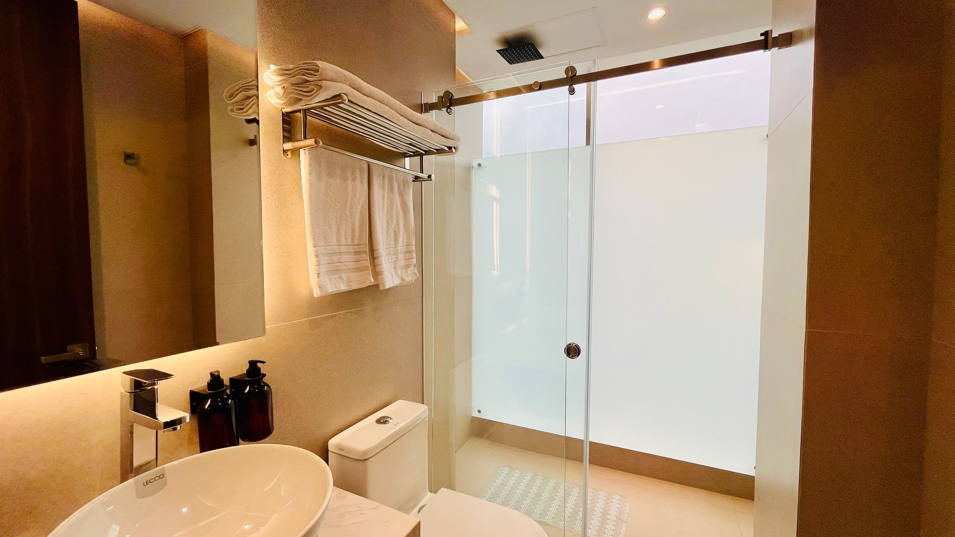 Un baño moderno con ducha envuelta en vidrio, un lavamanos blanco y un espejo sobre él.