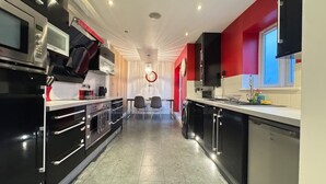 A modern kitchen with black appliances, a dining area with two chairs, and a red accent wall. - Spacious 2-Bedroom Duplex with Gated Parking (Doncaster)