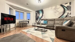 A modern living room with a large flat-screen TV, a sofa, a coffee table, and a wall mural. - Spacious 2-Bedroom Duplex with Gated Parking (Doncaster)