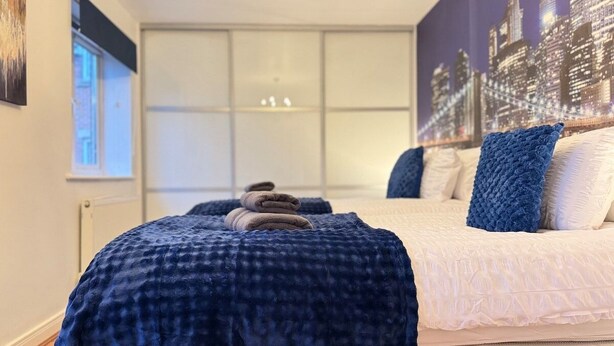 A bedroom with a bed, a blue blanket, and a cityscape mural on the wall. - Spacious 2-Bedroom Duplex with Gated Parking (Doncaster)