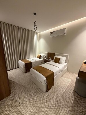 Ein modernes Hotelzimmer mit zwei Betten, einem großen Fenster mit Jalousien, einer Wand-Klimaanlage und einem strukturierten Teppich.