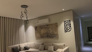 Uma sala de estar moderna com um sofá modular bege, uma mesa de centro de vidro e arte decorativa na parede, incluindo caligrafia árabe.