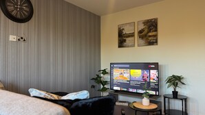 A modern hotel room with a large flat-screen TV, a striped wall, two paintings, a potted plant, and a small side table. - Stylish 2-Bedrooms | Free Gated Parking | 2 Bathrooms (Doncaster)