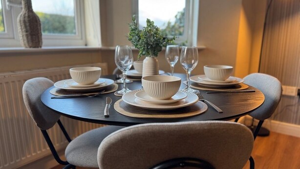 A round dining table with four chairs, white bowls, wine glasses, and a vase with greenery. - Stylish 2-Bedrooms | Free Gated Parking | 2 Bathrooms (Doncaster)
