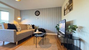 Ein modernes Wohnzimmer mit einer Couch, einem kleinen Tisch, einem Fernseher und einer Uhr an der Wand.