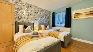 A hotel room with two beds, floral wallpaper, a window with curtains, and a painting on the wall. - Stylish 2-Bedrooms | Free Gated Parking | 2 Bathrooms (Doncaster)