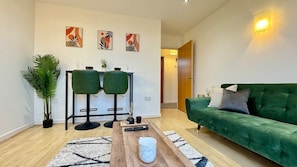 Una sala de estar moderna con un sofá verde, una mesa de centro, una mesita con dos sillas y una planta en maceta.