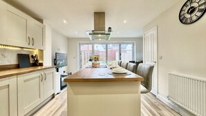 Een moderne keuken met een centraal eiland, witte kasten en een groot raam met uitzicht op buiten.