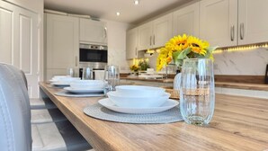 Een moderne keuken met witte kasten, een houten aanrechtblad en een eethoek met witte borden en glazen.