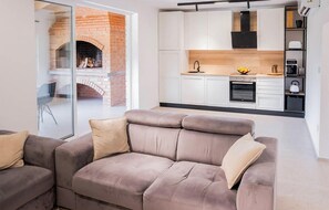 A modern living room with a grey sofa and a glass door leading to a kitchen with white cabinets and a brick fireplace. - Stunning home in Donji Velemeric with sauna (Donji Velemeric)