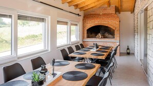 Une longue table à manger entourée de chaises noires, une cheminée en briques et de grandes fenêtres.