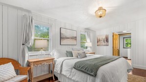 A bedroom with a bed, bedside tables, a chair, and artwork on the walls. - Cozy Cottage Mountain Retreat | The Glade Escape (Gatlinburg)