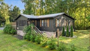 A cabin with a sloped roof, wooden exterior, and a brick foundation. It has a front porch with a staircase and is surrounded by a fenced yard with greenery. - Cozy Cottage Mountain Retreat | The Glade Escape (Gatlinburg)