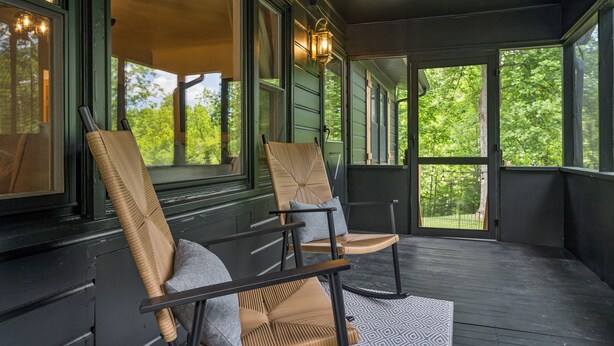 A porch with two wicker chairs, a patterned rug, and a view of greenery through large windows. - Cozy Cottage Mountain Retreat | The Glade Escape (Gatlinburg)