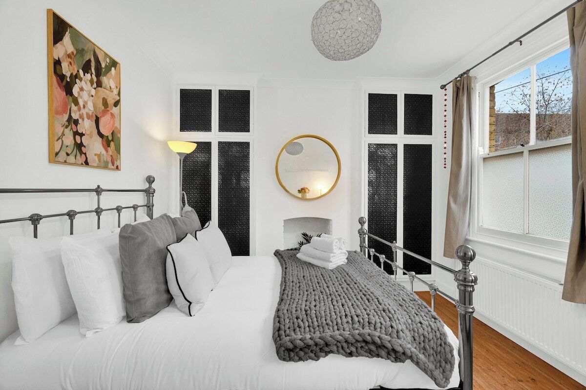 A bedroom with a bed, pillows, a blanket, a wall-mounted mirror, and a window with curtains.