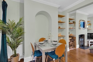 A dining area with a table set for four, surrounded by chairs with blue cushions. - Stylish 2BR House near Canary Wharf & Docklands (Greater London)