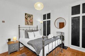 A bedroom with a bed, bedside table, lamp, and a large window with a view. - Stylish 2BR House near Canary Wharf & Docklands (Greater London)