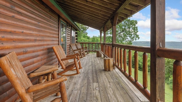 A wooden cabin with a porch featuring rocking chairs and a view of the surrounding forest. - Rustic Cedar Roost • Private Balcony • Best Views (Jasper)