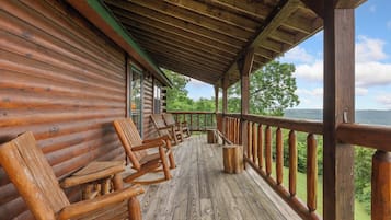A wooden cabin with a porch featuring rocking chairs and a view of the surrounding forest.