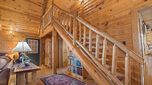 A wooden interior with a staircase, a lamp, a bookshelf, and a patterned rug. - Rustic Cedar Roost • Private Balcony • Best Views (Jasper)