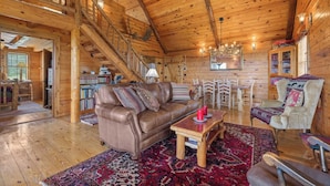 A cozy log cabin interior with a leather sofa, wooden dining table, and a staircase leading to an upper level. - Rustic Cedar Roost • Private Balcony • Best Views (Jasper)