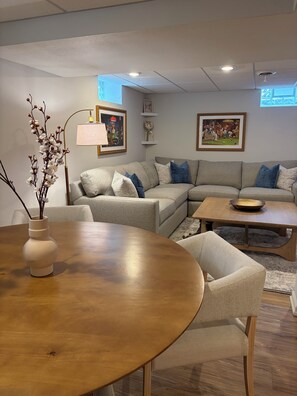 A living room with a round wooden table, a sofa set, a coffee table, and wall-mounted artwork. - Mid-Century Modern Themed Ranch-Styled Surprise House (Delafield)
