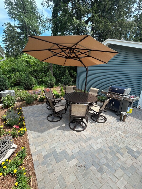 An outdoor patio with a round table, chairs, a grill, and an umbrella. - Mid-Century Modern Themed Ranch-Styled Surprise House (Delafield)