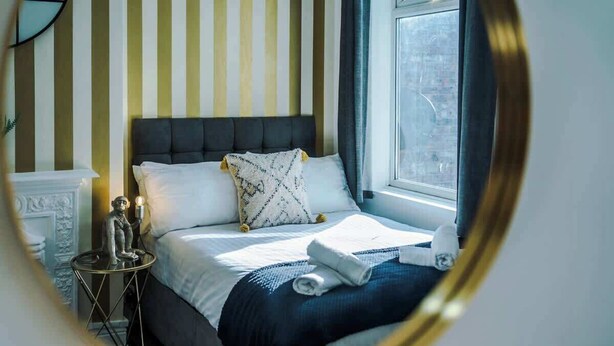 Un lit bien fait, avec un mur à rayures et une fenêtre en arrière-plan.