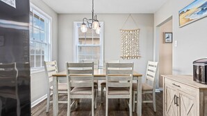 A dining area with a wooden table and chairs, a hanging light fixture, and a wall-mounted decorative piece. - 5BR Beach House in WW Crest - Sleep 12! (Wildwood)