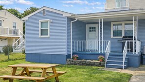 A two-story house with a front porch, a wooden picnic table, and a barbecue grill. - North WW 3BR Cottage Near Beach, Family-Friendly! (Wildwood)