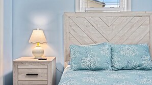 A bedroom with a wooden headboard, a bedside table with a lamp, and a bed with blue bedding featuring starfish and coral patterns. - North WW 3BR Cottage Near Beach, Family-Friendly! (Wildwood)