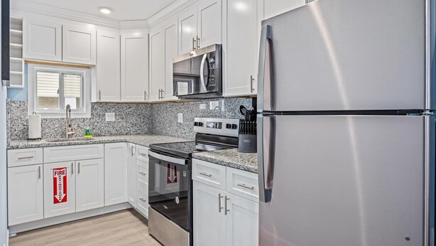 A modern kitchen with white cabinets, a stainless steel refrigerator, a microwave, an oven, and a sink with a faucet. - North WW 3BR Cottage Near Beach, Family-Friendly! (Wildwood)