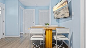 A dining area with a wooden table and white chairs, a white door, and a wall-mounted picture. - North WW 3BR Cottage Near Beach, Family-Friendly! (Wildwood)