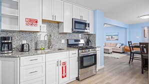A modern kitchen with white cabinets, granite countertops, stainless steel appliances, and a fire extinguisher sign. - North WW 3BR 1st Floor - Steps to the Beach! (North Wildwood)