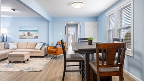 A living room with a beige sofa, a coffee table, and a rug. There is a dining area with a table and chairs. - North WW 3BR 1st Floor - Steps to the Beach! (North Wildwood)